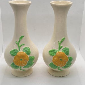 May include: A pair of white ceramic vases with yellow and green floral designs. The vases are about 7 inches tall and have a bulbous shape.