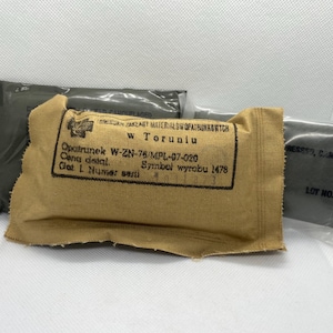 May include: A tan first aid kit with the text "Opatrunek W-ZN-76/MPL-07-020 Cana detal. Get L. Numer serti Symbol wyrobu 1478" printed on the front. The kit is wrapped in a clear plastic bag.