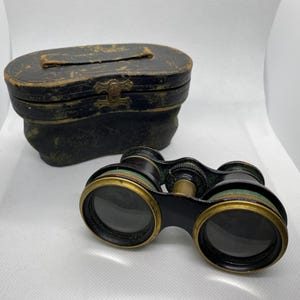 May include: Antique black and green opera glasses with a brass trim and a matching black leather carrying case.