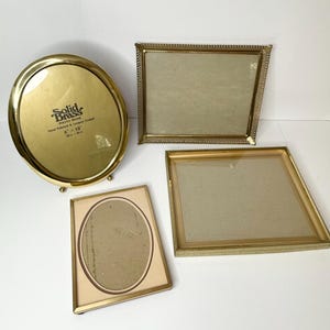 May include: Four vintage brass photo frames in various shapes. An oval frame with the text "Solid Brass Photo Frame" and dimensions of 8 x 10 inches. There are also three rectangular frames, each with a different design.
