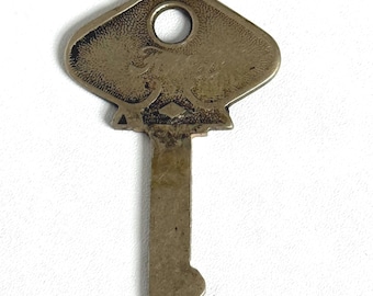 May include: A vintage metal key with a decorative head featuring an embossed design and a circular hole. The key has a rectangular stem with a notched end. The key is a tarnished silver color.