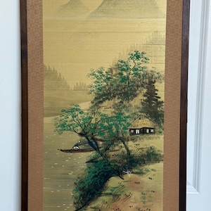 May include: A framed Japanese landscape painting featuring a river scene with mountains in the background. The artwork depicts a small boat, trees, and a traditional building. The painting is in a wooden frame with a gold and brown color scheme.