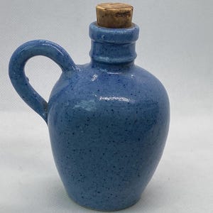 May include: A small blue ceramic jug with a cork stopper. The jug has a speckled glaze and a handle.