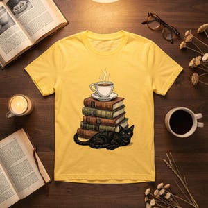 May include: A bright yellow t-shirt featuring a graphic illustration of a black cat lying in front of a stack of four hardback books, topped with a steaming white coffee cup and saucer. The design is centred on the front of the garment.