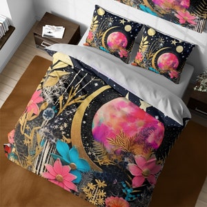 May include: A black and gold duvet cover with a pink and white moon and floral designs. The duvet cover is on a bed with two matching pillowcases.