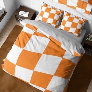 Op de afbeelding: Oranje en wit geruite beddengoedset met twee kussenslopen. Het beddengoed is gemaakt van zachte, comfortabele stof en heeft een gedurfd geruit patroon.