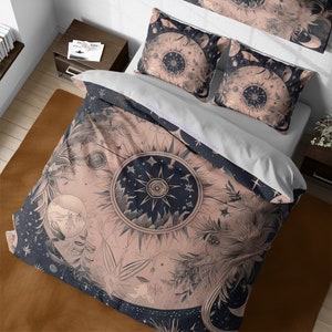 Op de afbeelding: Een roze en marineblauwe beddengoedset met een hemels zon- en maandesign. Het beddengoed heeft een herhalend patroon van sterren, planeten en bloemelementen. Het ontwerp is in vintage stijl met een zwart-wit kleurenschema.