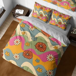 Puede incluir: Juego de cama con un diseño floral retro. La funda nórdica y las fundas de almohada muestran un patrón repetido de margaritas y otras flores en naranja, rosa, amarillo y azul. El texto "https://cozywhimsicals.etsy.com" es visible.