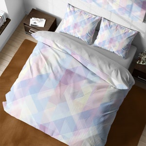 May include: A white duvet cover with a geometric pattern of pastel pink, blue, and yellow triangles. The duvet cover is on a bed with two matching pillowcases.