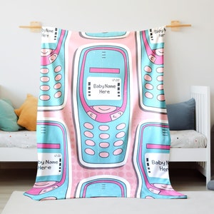 May include: A pink and blue baby blanket with a repeating pattern of retro cell phones. The cell phones have a pink and blue color scheme and the text "Baby Name Here" on the screen.