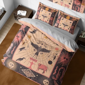 Op de afbeelding: Een roze en zwarte beddengoedset met een hemels ontwerp. De dekbedovertrek heeft een grote, ingewikkelde illustratie van een vogel met een ster op zijn borst, omringd door planeten, manen en sterren. De kussenslopen hebben kleinere hemelse ontwerpen.