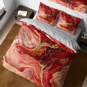 Può includere: Biancheria da letto con motivo a marmo rosso e oro con due federe a tinta unita. La biancheria da letto ha uno sfondo bianco con un motivo a marmo rosso e oro.