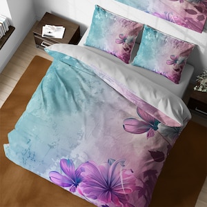 Peut inclure: Une housse de couette florale bleu sarcelle et rose avec un effet aquarelle. La housse de couette présente de grandes fleurs roses avec des centres blancs et des feuilles vertes. L'arrière-plan est un dégradé de bleu sarcelle et de rose.