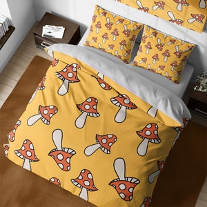 Può includere: Biancheria da letto gialla con un motivo a fungo bianco. I funghi hanno cappelli rossi con punti bianchi. La biancheria da letto è su un letto con cuscini bianchi e un copripiumino bianco.