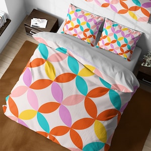 May include: A colourful bed set featuring a repeating pattern of overlapping circles in orange, pink, yellow, and teal on a white background. The set includes a duvet cover, two pillowcases, and a top sheet. The text "https://cozywhimsicaletsy.com" is visible.