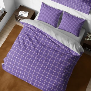 May include: Purple and white grid patterned bedding with a white duvet cover and two matching pillowcases. The bedding is on a brown surface.