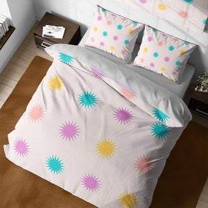 May include: White bedding with a pink, yellow, and turquoise star pattern. The bedding is made of soft, comfortable fabric and features a unique, whimsical design.