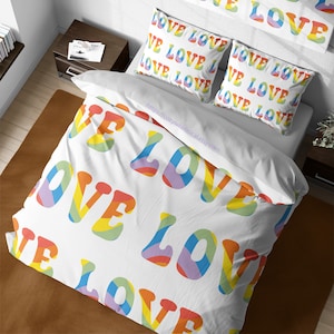 May include: White bedding with a rainbow pattern of the word "LOVE" repeated across the fabric. The bedding is shown on a bed with two matching pillowcases.