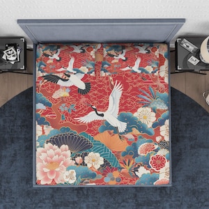 Puede incluir: Juego de cama con diseño de inspiración japonesa. La tela roja presenta grullas blancas, flores y nubes azules. La cama tiene un cabecero azul y está sobre una alfombra azul, inspirada en el arte tradicional japonés.