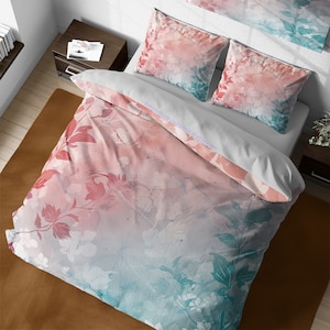 Pode incluir: Uma capa de edredom floral rosa e azul sobre um fundo branco. A capa de edredom apresenta um design em estilo aquarela com um degradê de rosa para azul. A capa de edredom é mostrada em uma cama com duas fronhas combinando.