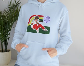 Puede incluir: Sudadera azul claro con un estampado gráfico de una persona sentada con una flor en un estilo retro. El gráfico presenta un arcoíris, un fondo verde y un sol morado.