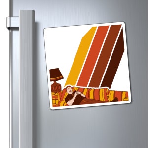 May include: A retro-style magnet featuring a man relaxing on a striped sofa with a lamp in the background. The background is a colourful striped pattern in shades of orange, yellow, and brown.