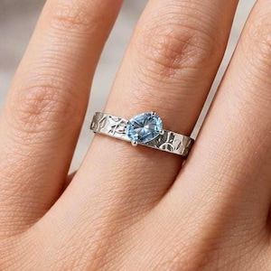 May include: A silver-toned ring featuring a central oval-cut light blue gemstone. The band has a textured, hammered-style surface with irregular indentations throughout the metal, creating a distinct pattern around the finger.