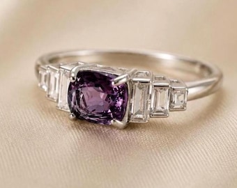 May include: A silver-toned ring featuring a central cushion-cut purple gemstone held by four prongs. The band is accented on each side by three clear, rectangular baguette-cut stones arranged in a stepped, graduated design along the metal shank.