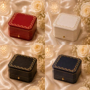May include: A set of four square jewellery boxes in red, white, black, and navy blue. Each box features a gold-toned latch and a decorative gold filigree border along the top edge. The boxes have a structured design with visible stitching details.