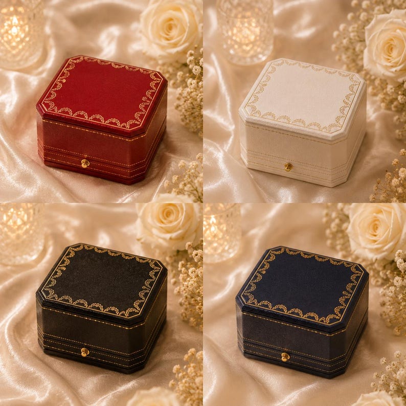 May include: A set of four square jewellery boxes in red, white, black, and navy blue. Each box features a gold-toned latch and a decorative gold filigree border along the top edge. The boxes have a structured design with visible stitching details.