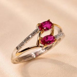 Può includere: Un anello bypass con due gemme ovali di un vivido colore rosa rossastro incastonate in griffe d'oro giallo. Il gambo diviso è realizzato in metallo argentato lucido, con un lato accentuato da una fila di piccole pietre chiare incastonate.