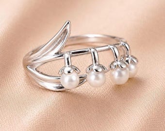 Könnte beinhalten: Ein silberfarbener Ring mit einem botanischen Design, das an ein Maiglöckchen erinnert. Die Ringschiene ist blattförmig geschwungen und trägt vier kleine, runde, weiße Perlen, die wie zarte Blüten nach unten hängen.