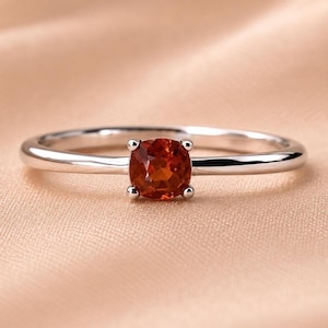 Könnte beinhalten: Ein Ring aus silberfarbenem Metall mit einem einzelnen, runden, facettierten orangefarbenen Edelstein in einer Vier-Krappen-Fassung. Die Ringschiene ist glatt und poliert und zeigt ein schlichtes Design, das die leuchtende Farbe des Steins betont.