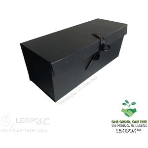 Op de afbeelding: Een zwarte rechthoekige geschenkdoos met bijpassende deksel, vastgebonden met een zwart lint. De doos heeft de tekst "VERSION VI-GRAND" en het Lexipoly-logo. De doos heeft ook de tekst "ONE ORDER, ONE TREE" en "LEXIBOX".