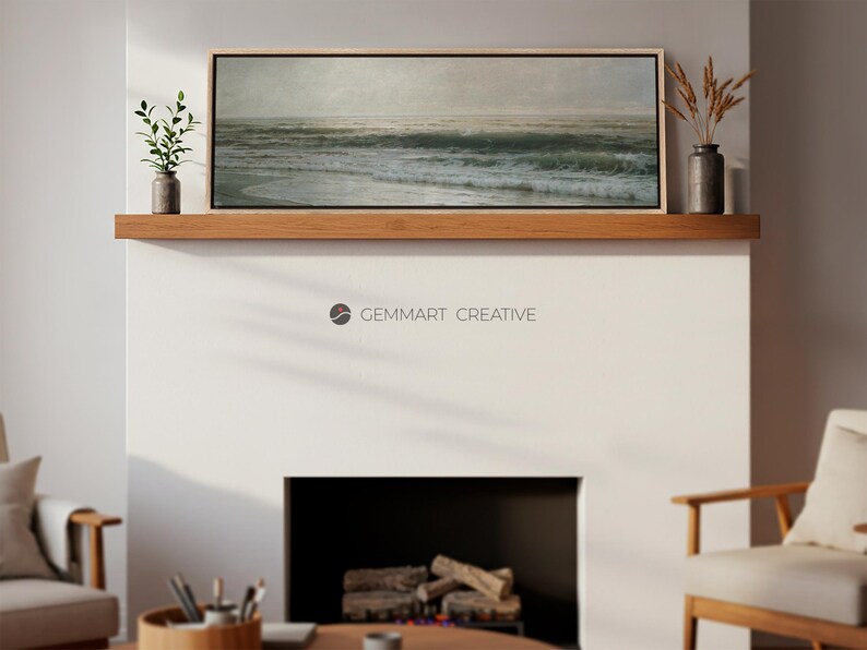 May include: A framed seascape painting with a light blue and green color scheme depicting a stormy ocean with waves crashing on the shore. The painting is hanging on a wooden shelf above a fireplace.