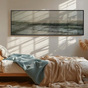 May include: A bedroom with a bed made with a light brown blanket and a light blue throw blanket. A black framed picture of a seascape hangs on the wall above the bed. A vase with dried pampas grass sits on a table in the corner of the room.