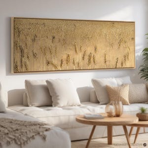 Puede incluir: Un arte de pared de lienzo de tono dorado que presenta un campo de tallos de trigo. La obra de arte se muestra sobre un sof&aacute; blanco con almohadas y una mesa de caf&eacute;.