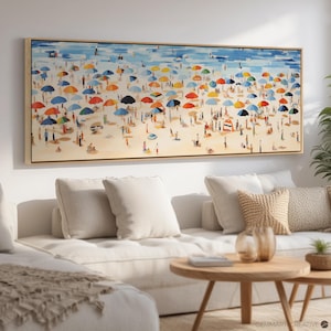 Può includere: Un dipinto colorato di una scena di spiaggia con molte persone sotto gli ombrelloni. Il dipinto è in una cornice di legno ed è appeso a una parete bianca sopra un divano bianco.