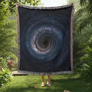 May include: A woven throw blanket featuring a dark blue galaxy print with a swirling black hole in the center.