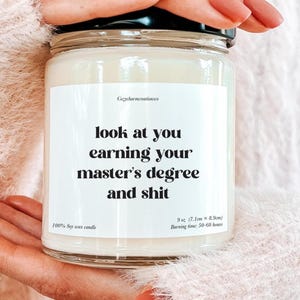 Puede incluir: Una vela en tarro de cristal transparente con tapa negra. La vela tiene una etiqueta blanca con el texto "look at you earning your master's degree and shit". La vela mide 7,1 cm x 8,9 cm y está hecha de cera de soja 100%. Tiempo de combustión: 50-60 horas.
