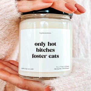 May include: A soy wax candle in a glass jar with a black lid. The label reads "only hot bitches foster cats" in black text. The candle is 9 oz (7.1cm x 8.5cm) and has a burning time of 50-60 hours.