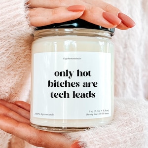 以下が含まれることがあります： 黒い蓋が付いたガラス瓶に入った白い大豆ワックスキャンドル。ラベルには「only hot bitches are tech leads」と書かれています。キャンドルのサイズは7.1cm x 8.9cmで、燃焼時間は50〜60時間です。