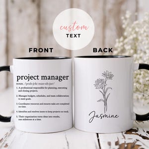 Op de afbeelding: Witte keramische mok met een zwarte binnenkant en handvat. De voorkant toont de tekst "project manager" met een definitie. De achterkant toont een bloemenillustratie en de naam "Jasmine".
