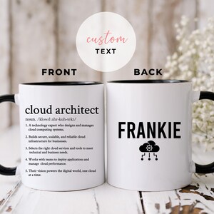 May include: White ceramic coffee mug with a black rim and handle. The front of the mug has the definition of a cloud architect. The back of the mug has the name Frankie and a cloud icon with a gear inside.