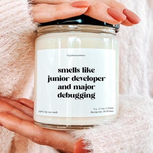 Könnte beinhalten: Ein Glas-Kerzenglas mit schwarzem Deckel. Das Etikett lautet "smells like junior developer and major debugging". Die Kerze ist 7,1 cm x 8,9 cm groß und besteht aus 100 % Sojawachs mit einer Brenndauer von 50-60 Stunden.