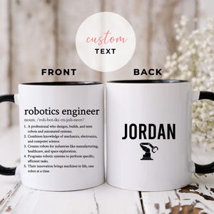 Puede incluir: Taza de cerámica blanca con interior, asa y borde negros. La parte delantera presenta el texto "robotics engineer" con una definición. La parte trasera muestra el nombre "JORDAN" y un gráfico de brazo robótico.