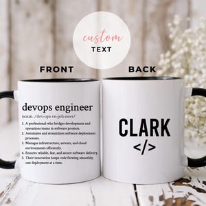 May include: White ceramic mug with a black handle and rim. The front has the text "devops engineer" and a definition. The back of the mug displays the name "CLARK" and code symbols.