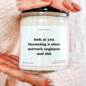 May include: A glass jar candle with a black lid. The label reads "look at you becoming a cisco network engineer and shit." The candle is 9 oz (7.1cm x 8.9cm) and made of 100% soy wax, with a burning time of 50-60 hours.