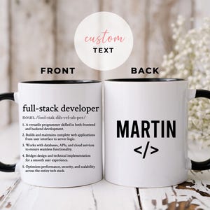 Puede incluir: Taza de café de cerámica blanca con borde y asa negros. La parte delantera de la taza tiene la definición de "desarrollador full-stack" impresa en texto negro. La parte trasera de la taza tiene el nombre "MARTIN" impreso en texto negro con corchetes angulares.