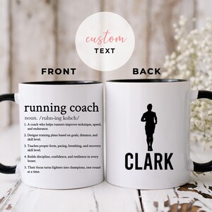 May include: White ceramic mug with a black interior, handle, and text. The front reads "running coach" with a definition. The back features a runner silhouette and the name "Clark".